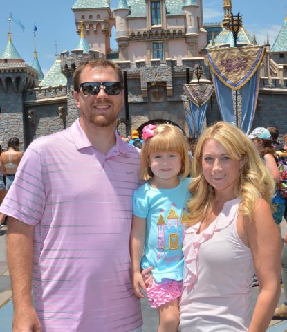 Kristen Z with her husband and daughter in front of the castle at Disney