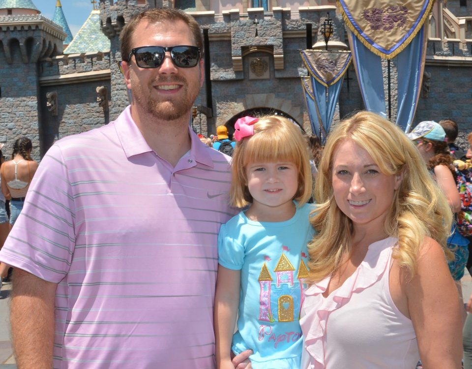 Kristen Z with her husband and daughter in front of the castle at Disney