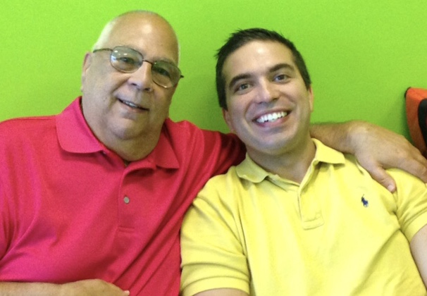 Michael Fera and his son wearing vibrant colors against a green wall