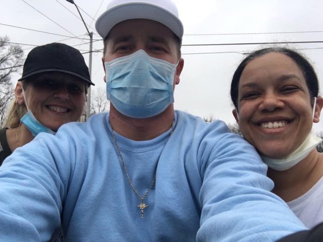 Shawn Wright wearing a blue sweatshirt and cross necklace while wearing a mask next to friends