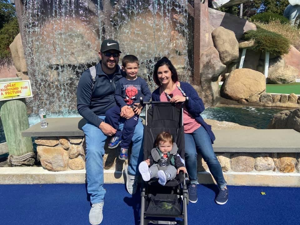 christie vlk with her husband and two kids sitting in front of a waterfall at a mini golf course