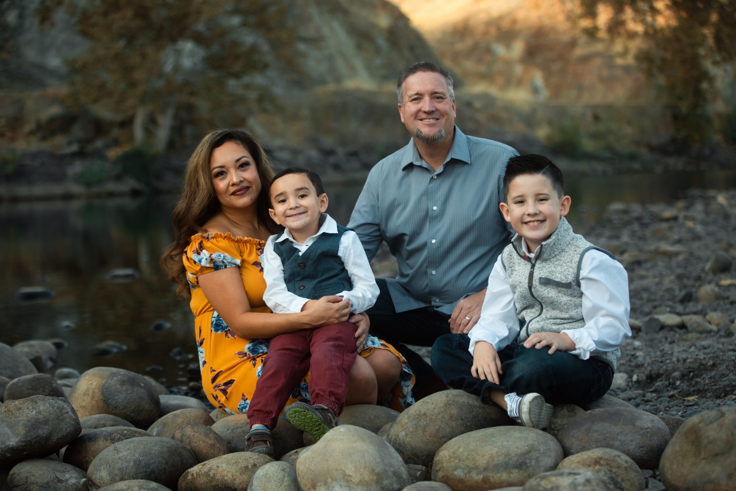 Valarie Melton with her husband and their two young boys sitting on the rocks by the river