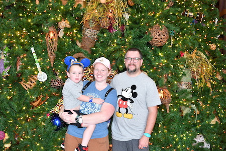 Michelle Wilson with her husband and son wearing Disney shirts in front of the Disney Christmas tree
