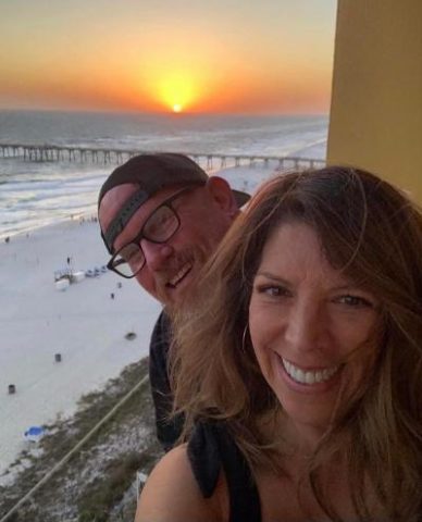 Marydawn and Rick Kornmeier on the balcony at the beach with the sunset and the pier in the background