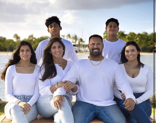 Lindsey Suárez withe her husband and four children wearing white tops and jeans in front of the water