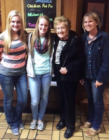 Angie Probst and her daughter and granddaughters in front of a neon menu sign