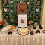 A framed story titled 'Generosity & Wisdom' sitting as the centerpiece of an 80th birthday party cake table