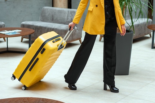 A woman wheeling a yellow suitcase.