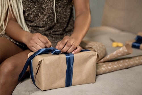 A woman packing a gift with a blue ribbon.