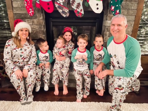 Jane Jewett with her husband and children wearing matching Christmas pajamas in front of the fireplace
