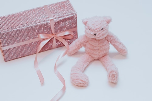 prink yarn crochet teddy bear sitting next to pink gift box