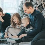 family flipping through a book in front of a Christmas tree