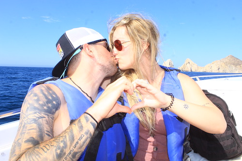 Cody and Amber in vests on a boat making hand hearts