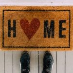 a person standing in front of the door mat saying home