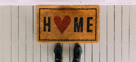 a person standing in front of the door mat saying home